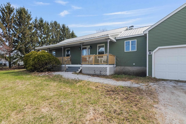 view of front facade with a porch, metal roof, an attached garage, dirt driveway, and a front yard