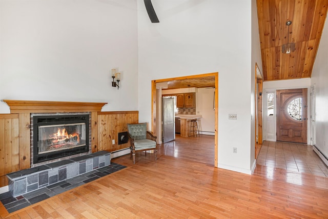 entrance foyer with high vaulted ceiling, a tiled fireplace, a baseboard heating unit, and light wood-style flooring
