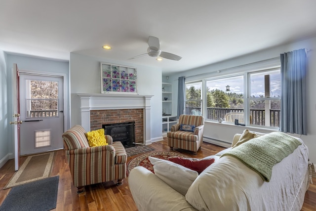 living area with a baseboard heating unit, wood finished floors, a fireplace, and ceiling fan