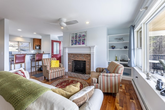 living area featuring a baseboard heating unit, dark wood-style floors, recessed lighting, ceiling fan, and a fireplace