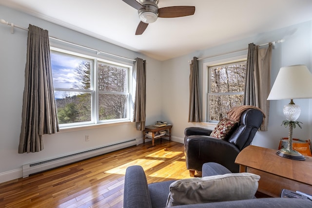 sitting room featuring a baseboard heating unit, ceiling fan, a wealth of natural light, and wood finished floors