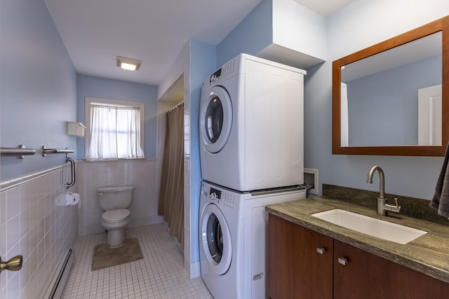 bathroom featuring stacked washer and clothes dryer, tile patterned floors, toilet, vanity, and tile walls