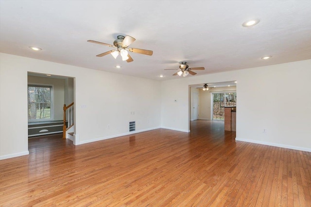 spare room featuring stairway, a ceiling fan, light wood finished floors, and plenty of natural light