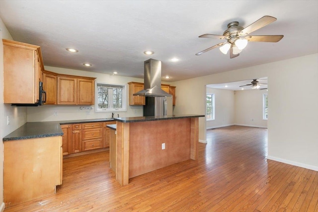 kitchen with light wood-style floors, dark countertops, island range hood, and a center island
