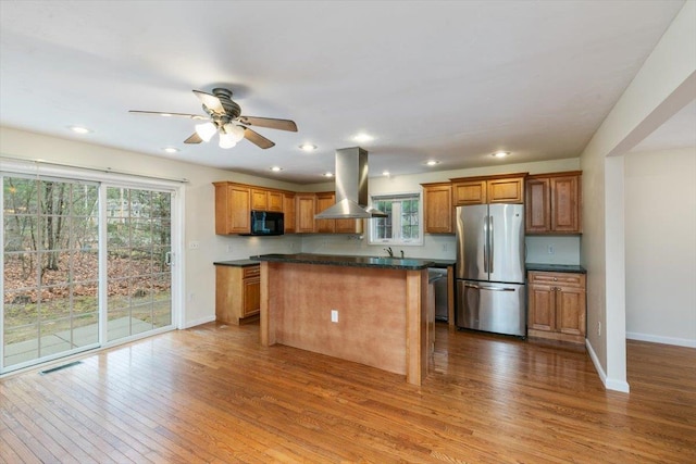 kitchen with island exhaust hood, black microwave, wood finished floors, and freestanding refrigerator