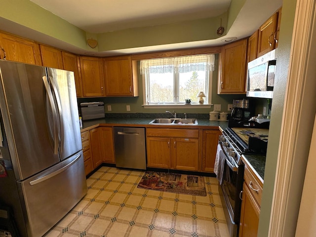 kitchen featuring dark countertops, a sink, brown cabinetry, light floors, and stainless steel appliances