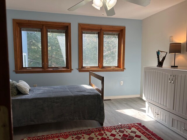 bedroom with ceiling fan, baseboards, multiple windows, and light wood-style floors