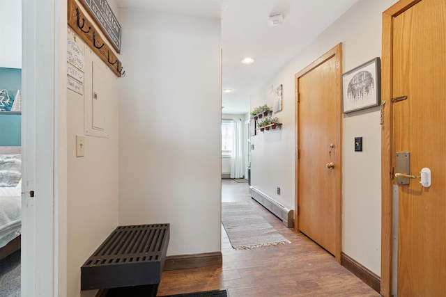 corridor with baseboard heating, baseboards, wood finished floors, and recessed lighting