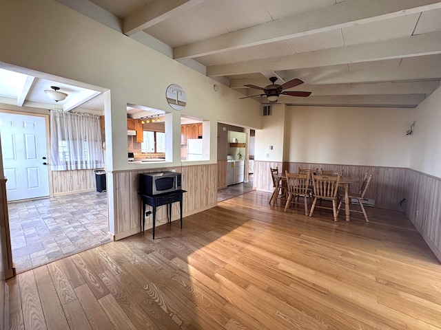 dining space featuring wood finished floors, wainscoting, wooden walls, ceiling fan, and beam ceiling
