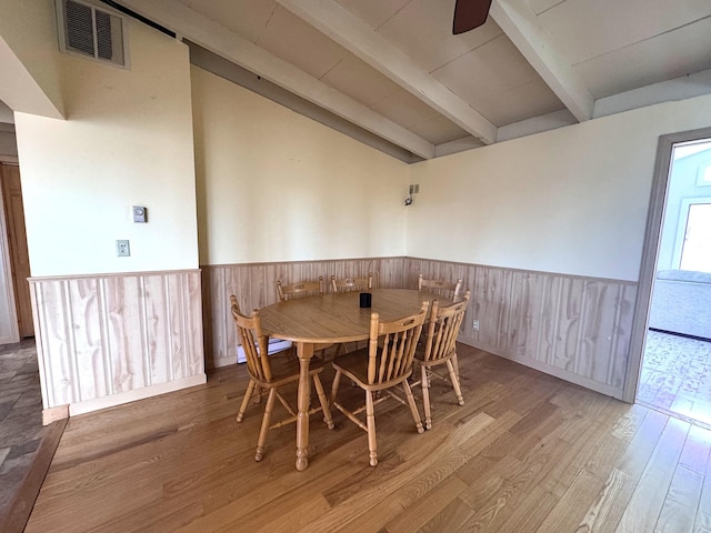dining room featuring wood finished floors, visible vents, vaulted ceiling with beams, wainscoting, and ceiling fan