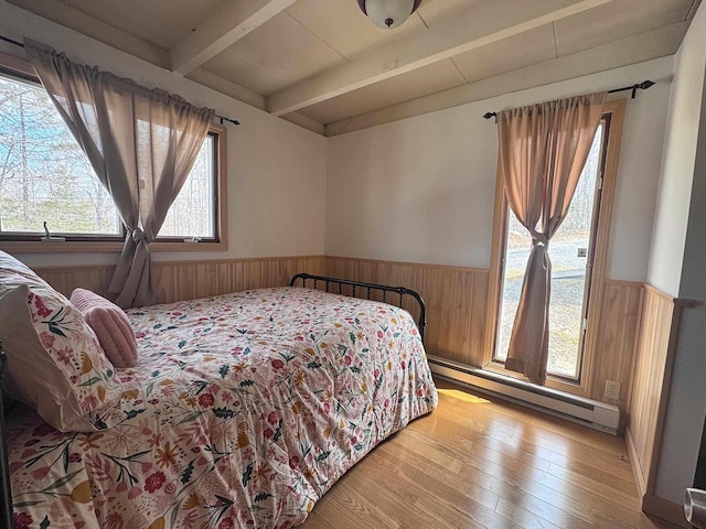 bedroom with beam ceiling, wainscoting, wooden walls, hardwood / wood-style flooring, and a baseboard radiator