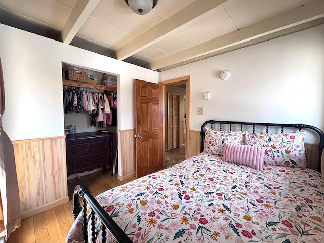 bedroom with beamed ceiling, wood finished floors, a wainscoted wall, and wood walls