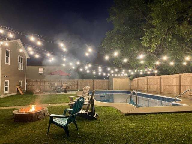 pool at night with a fenced backyard, a yard, a fenced in pool, and an outdoor fire pit