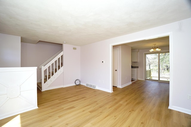unfurnished room with baseboards, visible vents, an inviting chandelier, light wood-style floors, and stairs