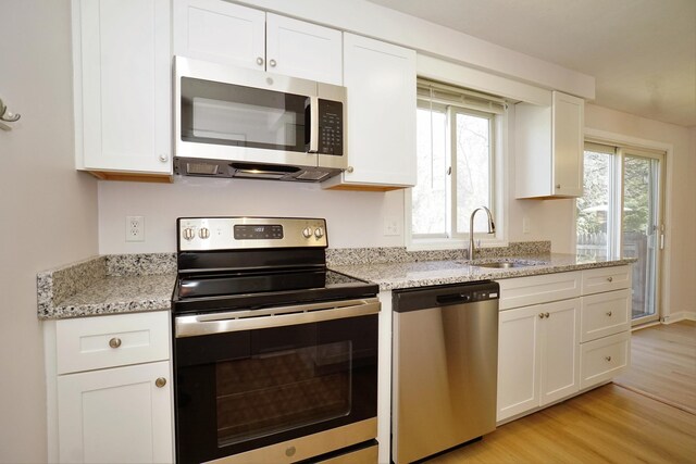 kitchen with stainless steel appliances, light wood-style flooring, a sink, white cabinetry, and light stone counters