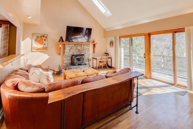 living area featuring light wood-type flooring, a wood stove, a skylight, and high vaulted ceiling