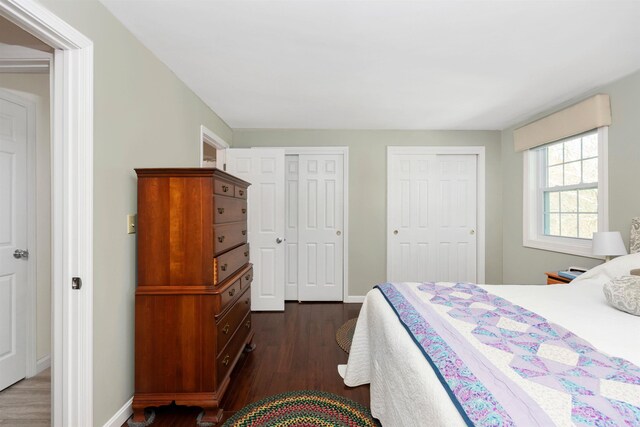 bedroom with two closets, baseboards, and dark wood-type flooring