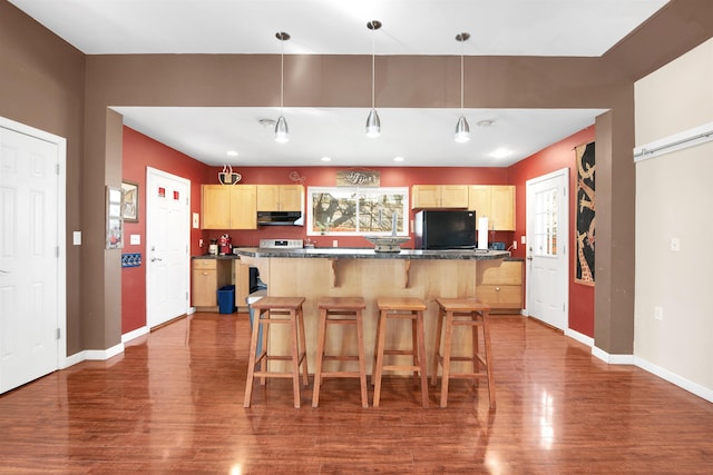 417 Locust St, Rollinsford, NH 03869 - kitchen with freestanding refrigerator, under cabinet range hood, dark wood-style floors, light brown cabinetry, and a kitchen breakfast bar