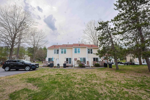 back of house with a wooden deck, uncovered parking, and a lawn
