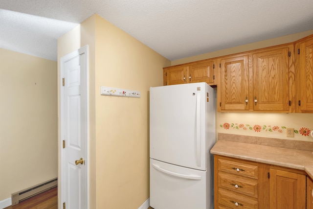 kitchen featuring brown cabinets, light countertops, a textured ceiling, baseboard heating, and freestanding refrigerator