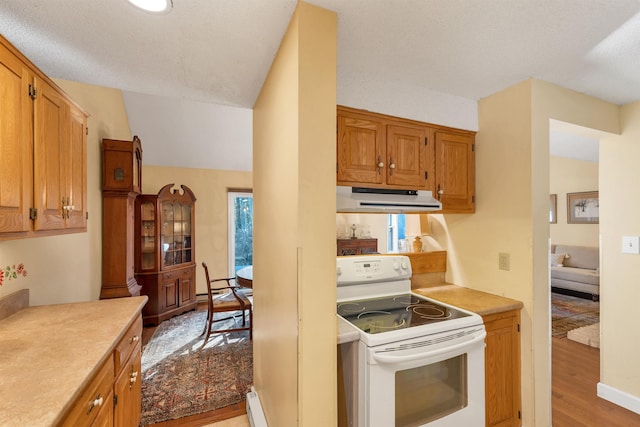 kitchen with electric stove, under cabinet range hood, brown cabinetry, light wood-style flooring, and light countertops