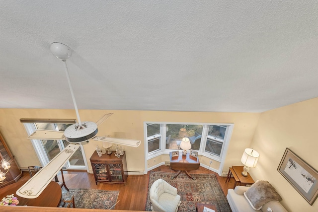 living area featuring a baseboard heating unit, a textured ceiling, wood finished floors, and baseboards