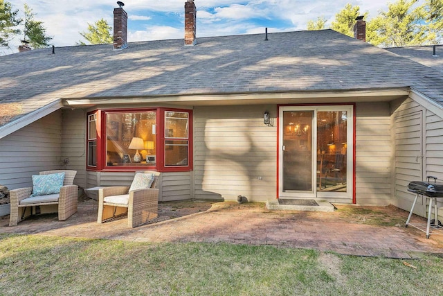rear view of property featuring a patio, a shingled roof, and a chimney