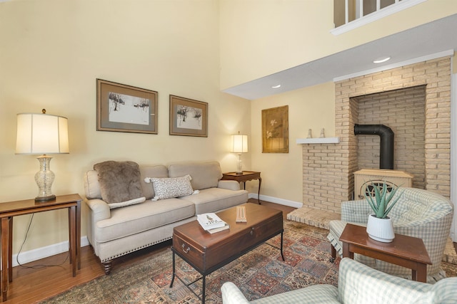 living room with a wood stove, a towering ceiling, wood finished floors, and baseboards