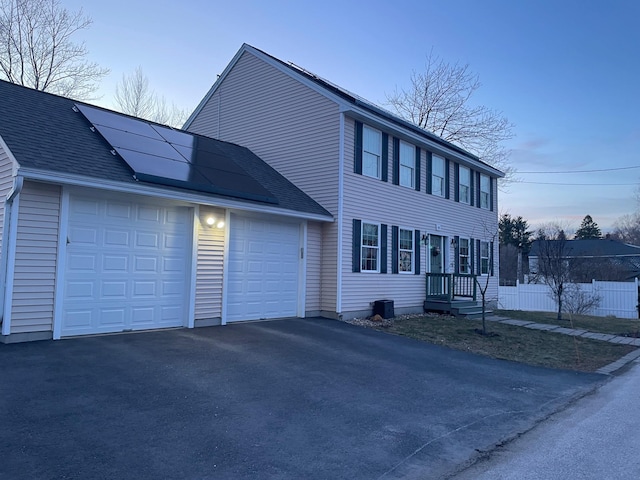 colonial house featuring driveway, fence, solar panels, and a garage