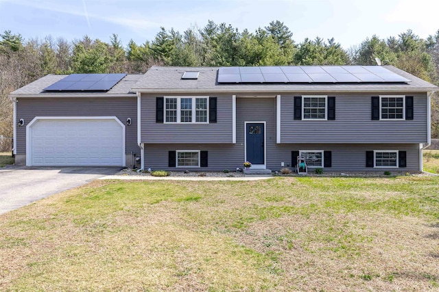 raised ranch featuring roof mounted solar panels, driveway, a front yard, and entry steps