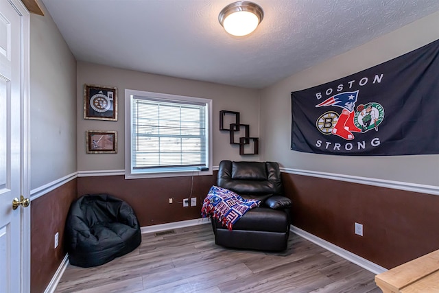 living area with baseboards, visible vents, wood finished floors, and a textured ceiling