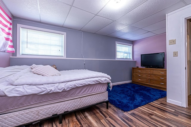bedroom with baseboards, wood finished floors, and a drop ceiling