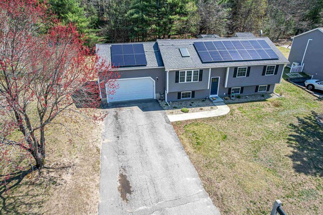 raised ranch featuring driveway, roof mounted solar panels, roof with shingles, a front yard, and an attached garage