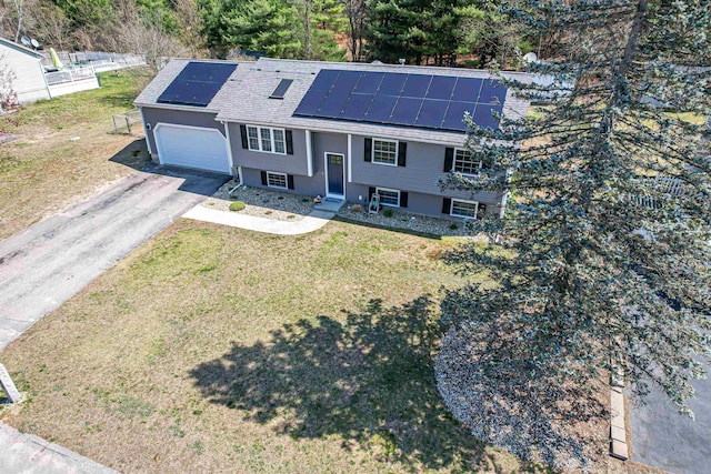 split foyer home with aphalt driveway, a garage, roof mounted solar panels, roof with shingles, and a front lawn