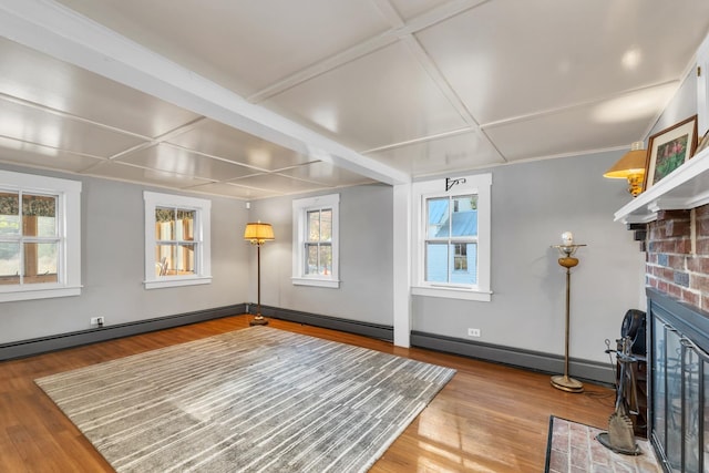 unfurnished living room with wood finished floors, baseboards, baseboard heating, and a brick fireplace