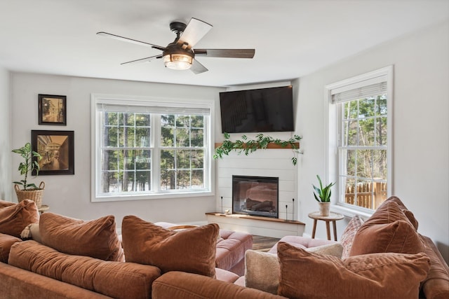 living area with ceiling fan, a wealth of natural light, and a glass covered fireplace