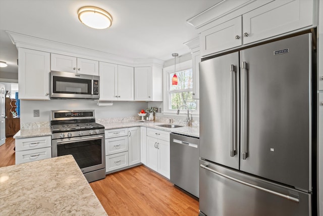 kitchen with light stone countertops, appliances with stainless steel finishes, light wood finished floors, a sink, and white cabinetry