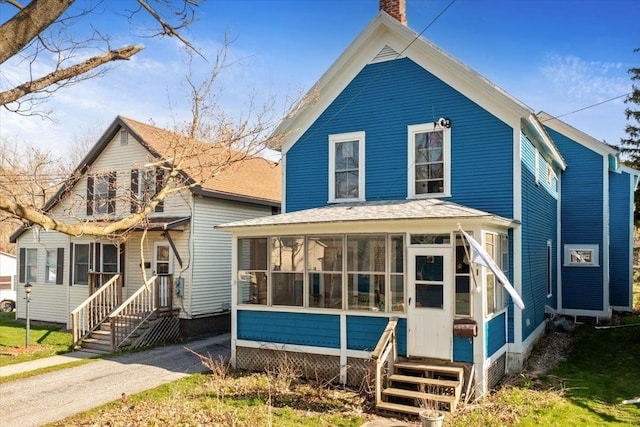 view of front of house featuring a chimney, entry steps, and a sunroom