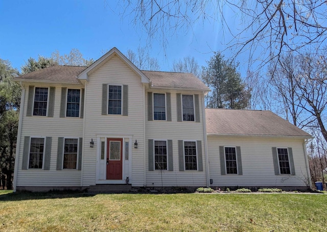 colonial house featuring roof with shingles and a front yard