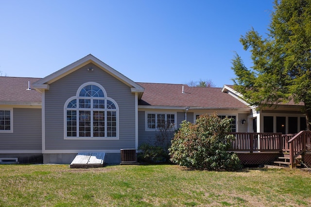 rear view of property with cooling unit, a wooden deck, a yard, and a shingled roof