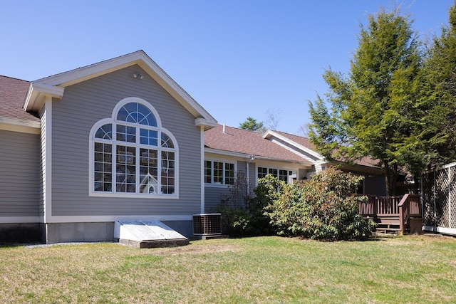 view of side of property with a deck, a yard, roof with shingles, and central AC unit
