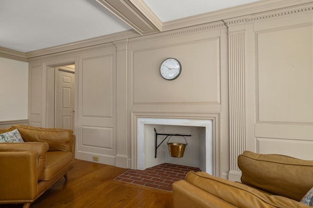 living area featuring wood finished floors, a decorative wall, and ornamental molding