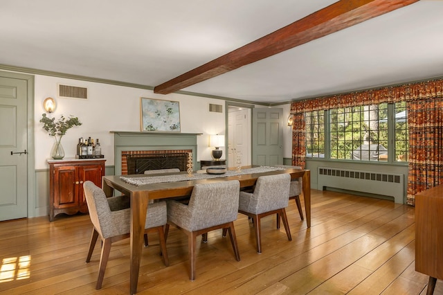 dining space with visible vents, radiator heating unit, beam ceiling, and light wood-style flooring