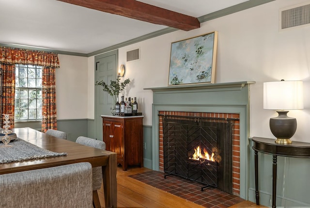 living area with a fireplace, visible vents, beamed ceiling, and wood-type flooring