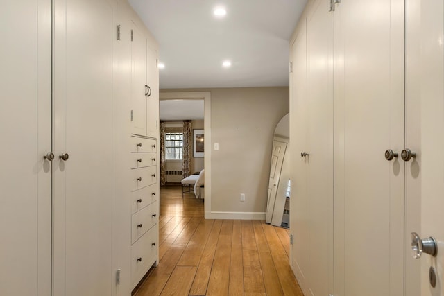 hallway with radiator, light wood finished floors, recessed lighting, baseboards, and arched walkways