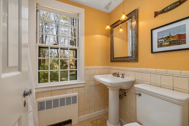 bathroom featuring tile walls, radiator heating unit, a healthy amount of sunlight, and wainscoting