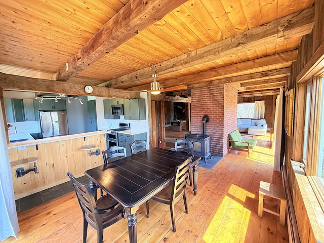 dining space with wood ceiling, light wood-type flooring, beamed ceiling, and a wood stove