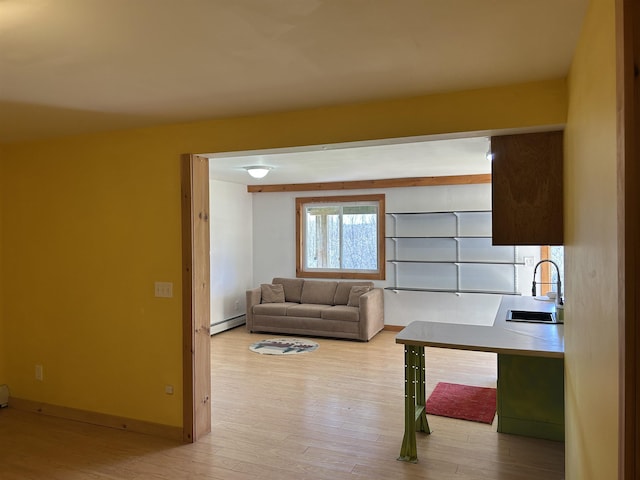 living room with a baseboard heating unit, light wood-style flooring, and baseboards