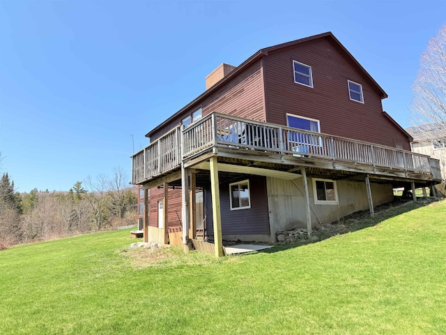 rear view of property with a chimney, a wooden deck, and a lawn