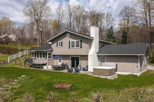 back of house featuring a lawn, a patio, a chimney, and a hot tub